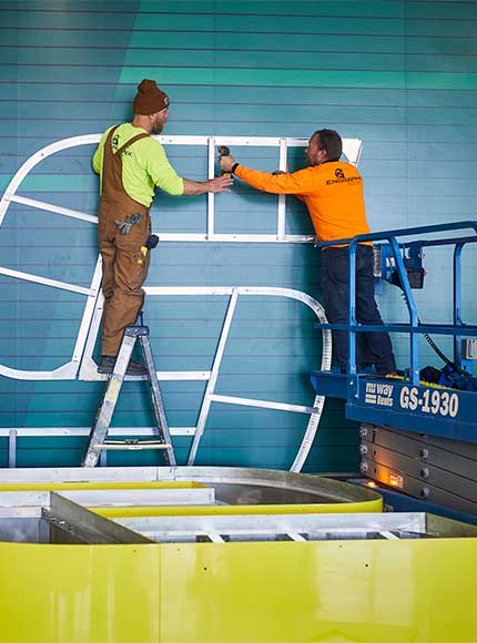2 employees at Sign Installation company installing large letter at high school