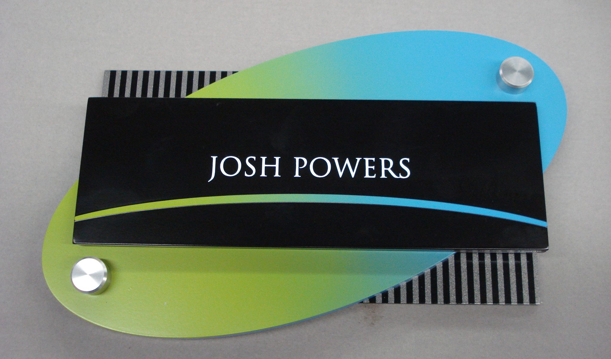 Blue and green gradient oval against striped rectangle featuring employee name for office sign