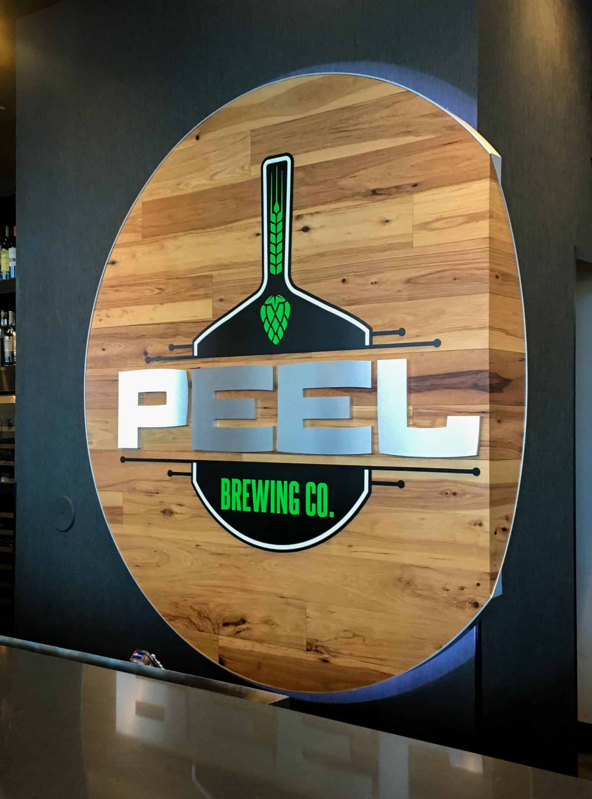 Wood circle backing to peel pizza branded logo wall with brush aluminum letters and black and green pizza peel